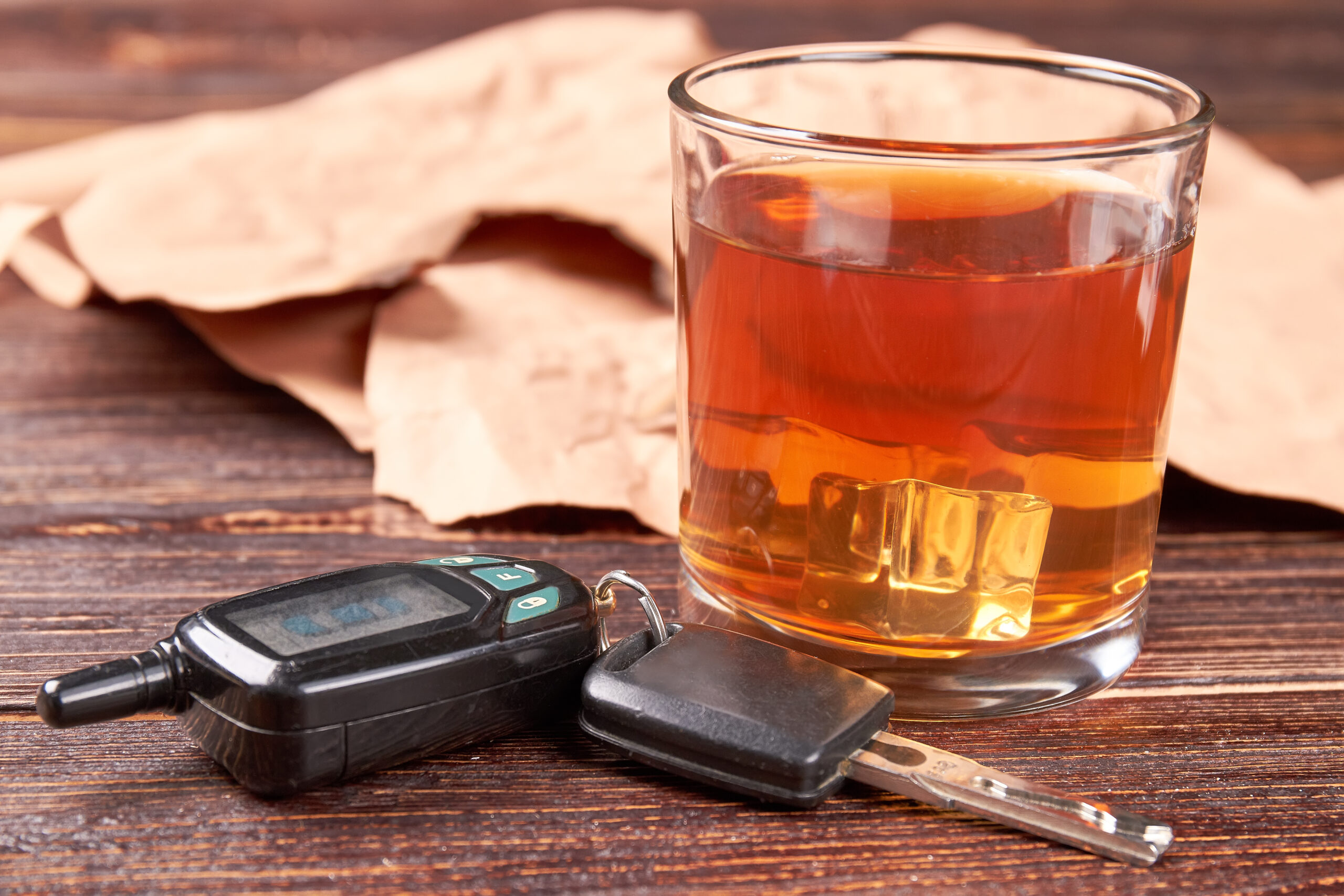 Glass of whisky, car keys, paper. Alcohol in transparent glass, automobile keys, vintage paper on wooden background.